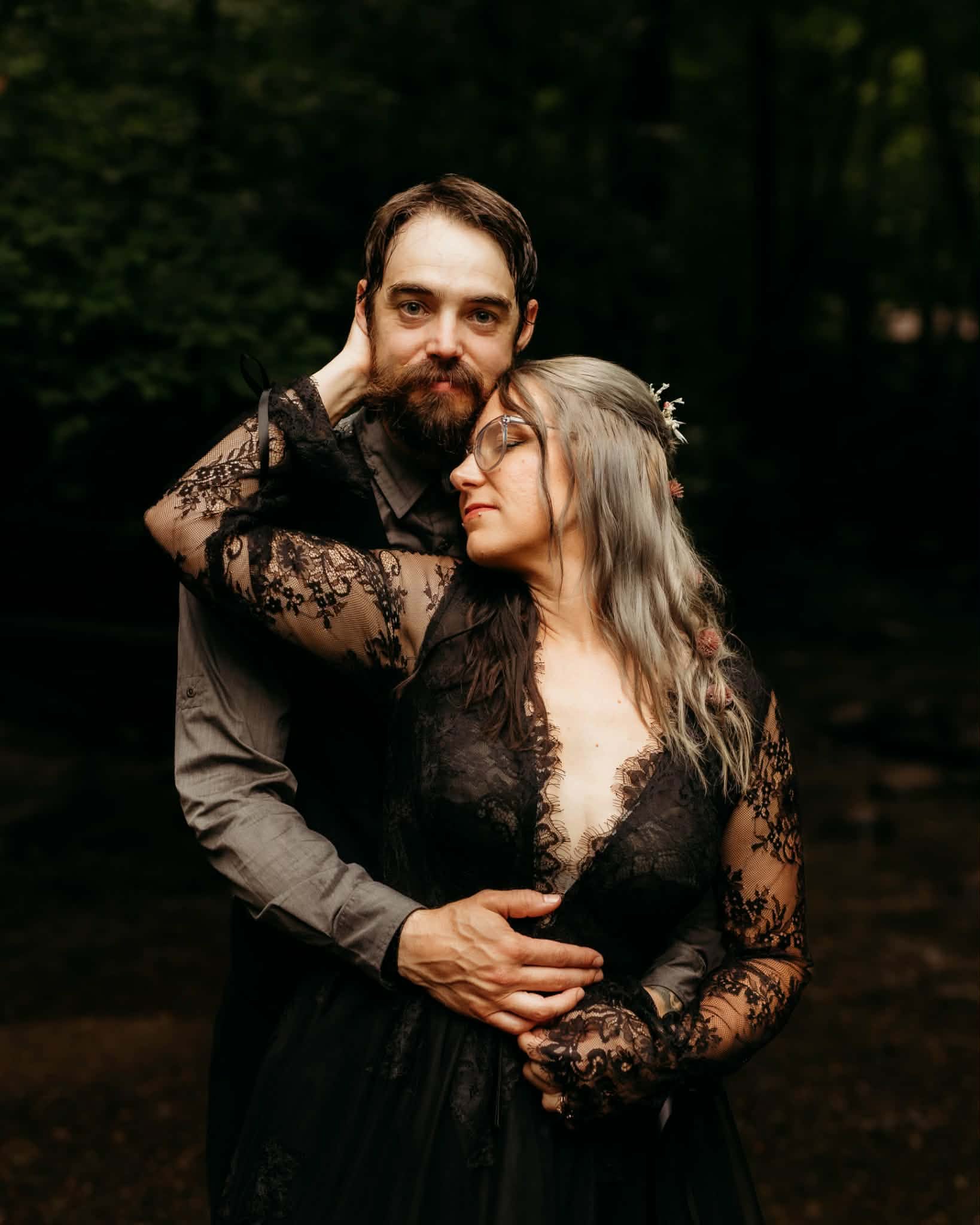 Tattooed bride and bearded groom embracing in a forest
