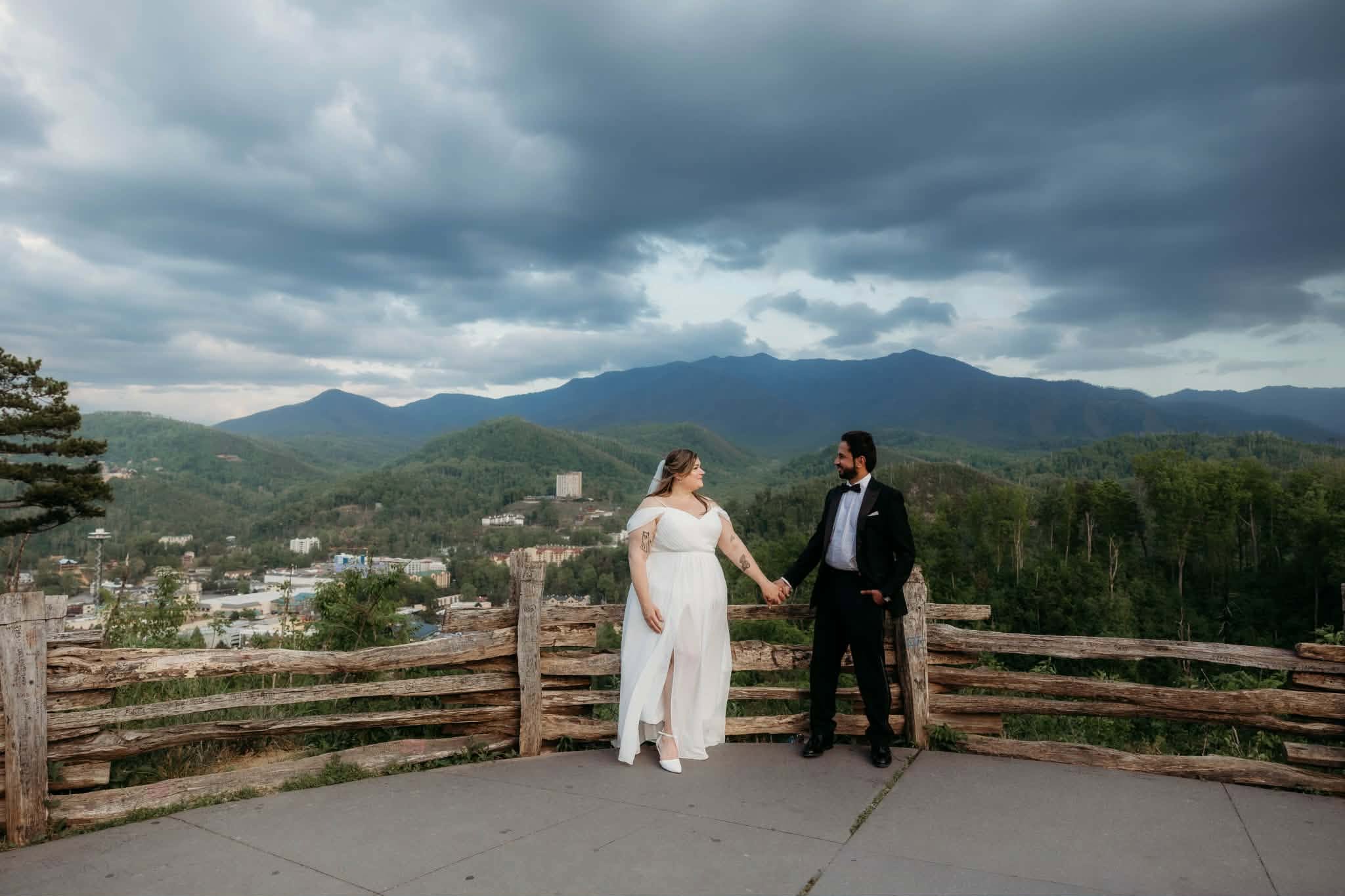 Bride and groom standing at a mountain overlook beneath dramatic clouds