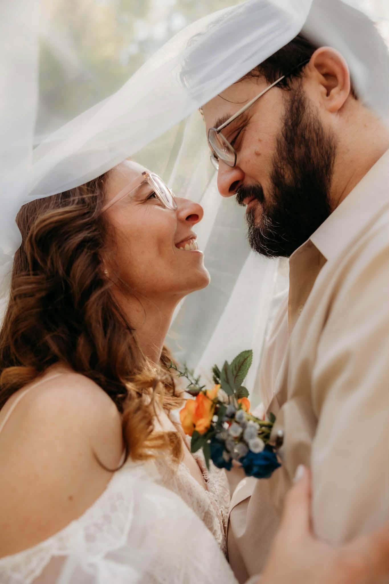 Newlyweds smiling at one another beneath the bride's veil