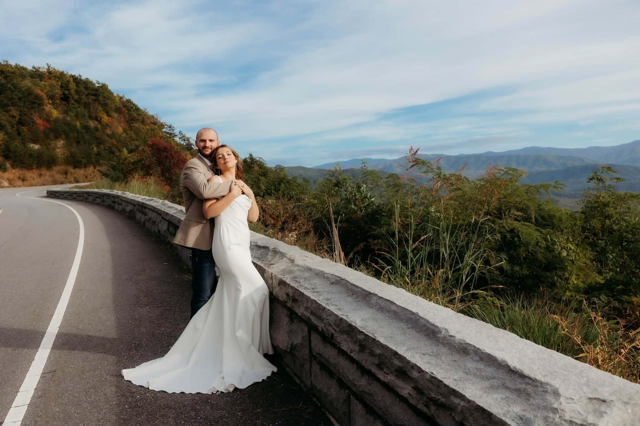 Couple embracing beside a stone wall with mountains beyond