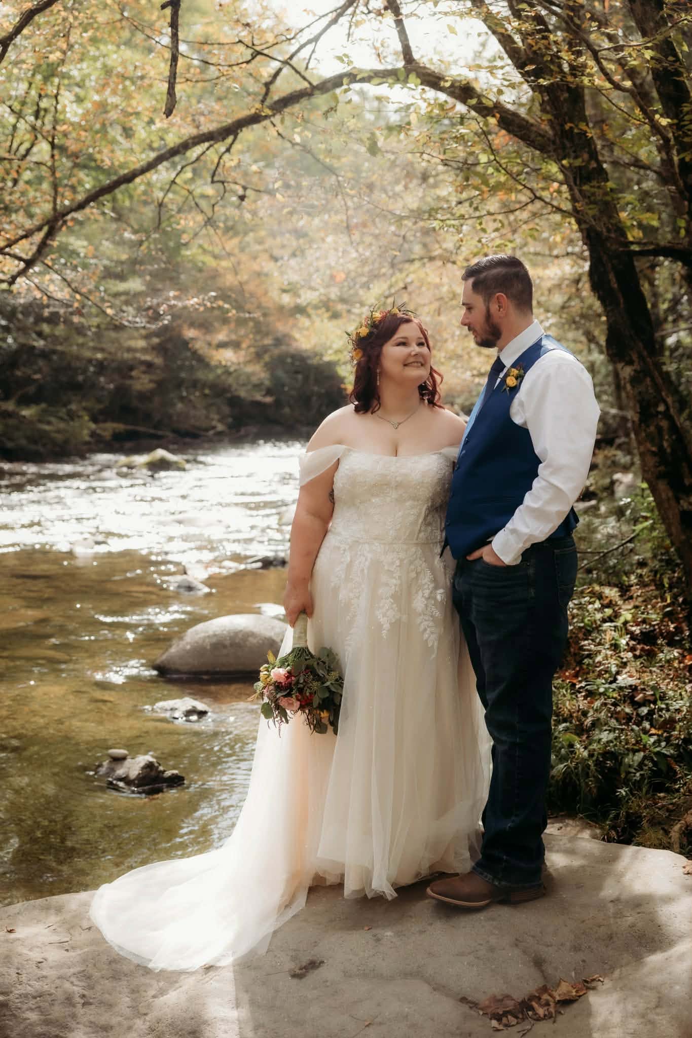 Newlyweds standing together beside a rocky stream