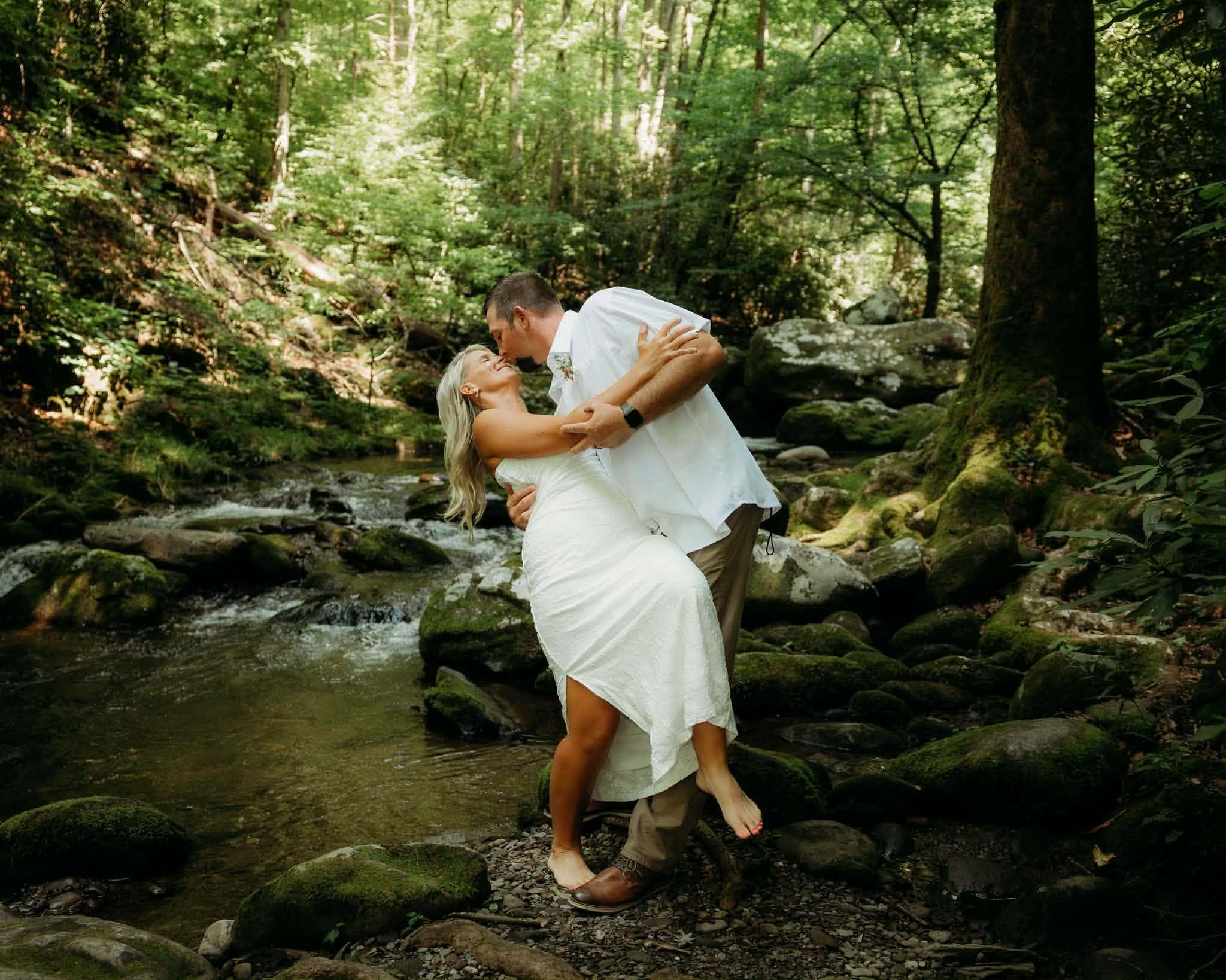 Groom dipping his bride beside a forest creek