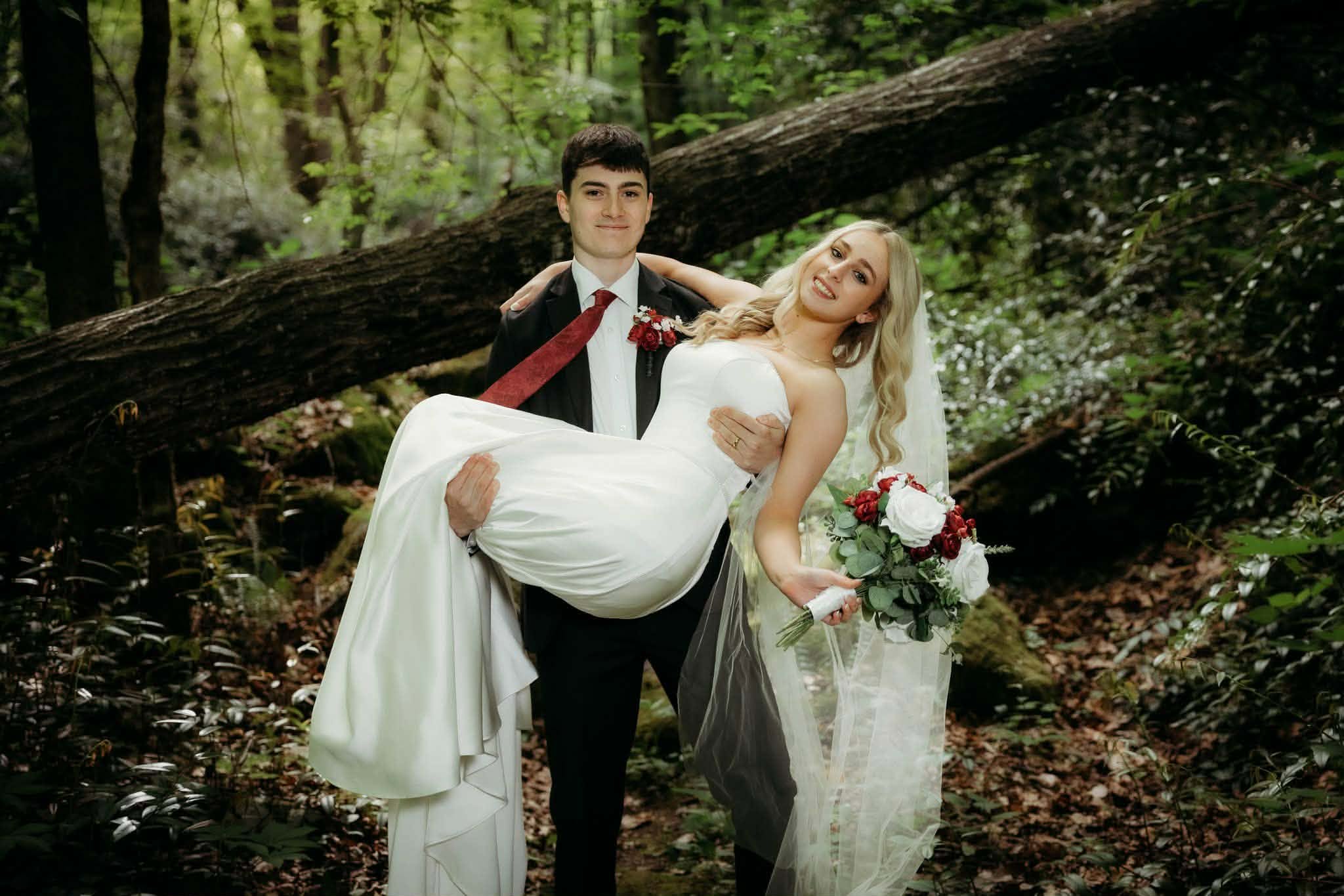 Groom carrying his smiling bride through the forest