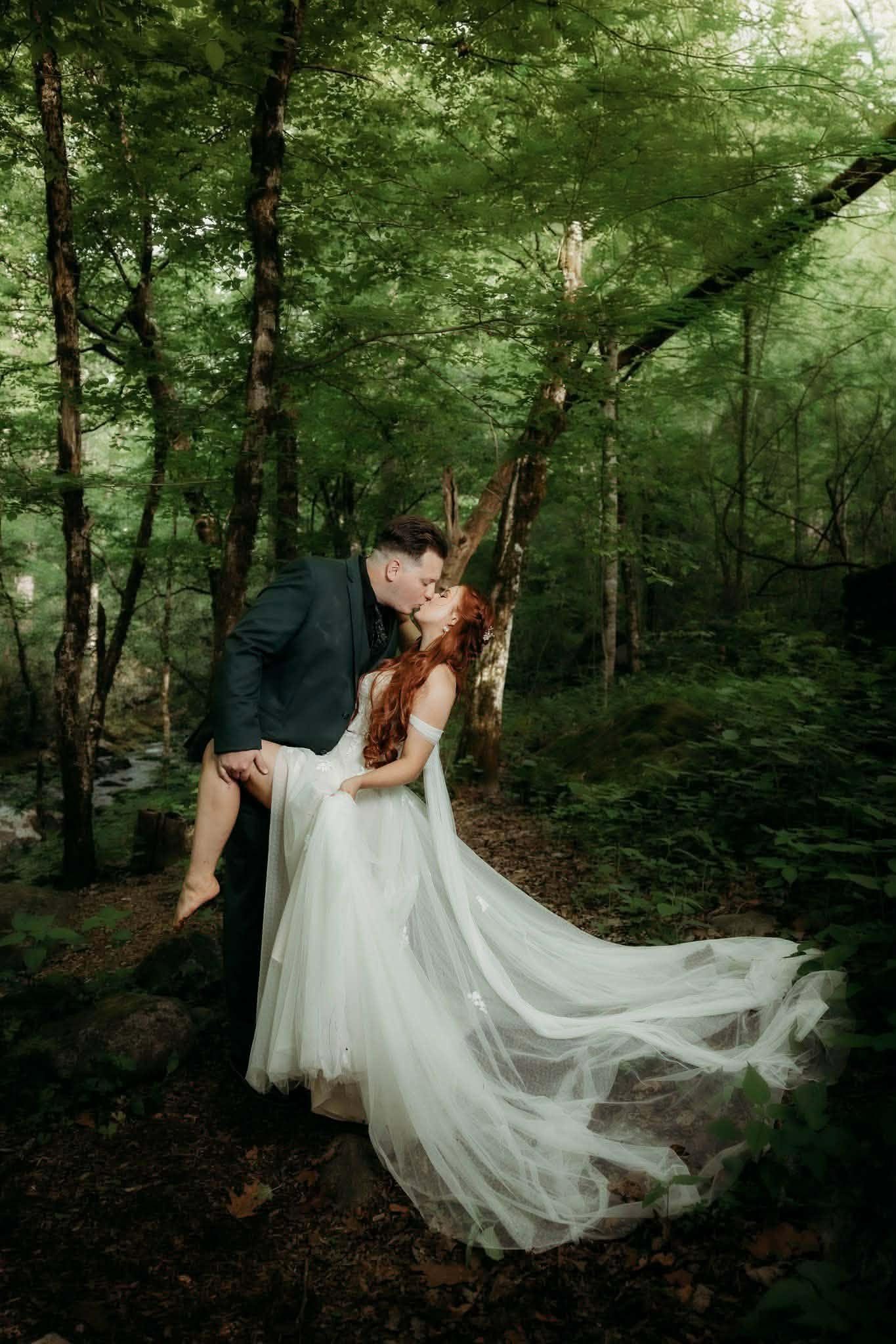 Groom kissing his bride among tall forest trees